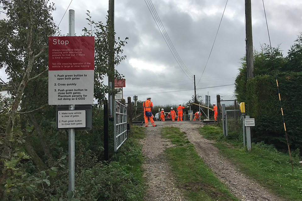 View of the approach to Frognal Farm user worked crossing showing a red and white Stop sing, the crossing phone and gate. A number of railworkers in high visibility clothing are on the scene.