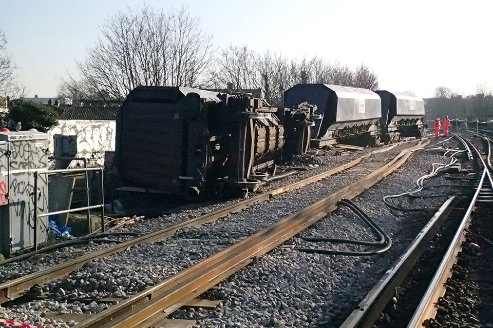 Winter view of the derailment at Lewisham showing one vehicle on its side to the left and two vehicles upright but standing in the ballast.