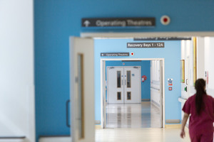 A nurse walking down a hospital corridor with a sign to the operating theatre.