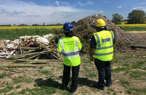 EA and HMRC officers stand in front of a pile of waste on an illegally operating site