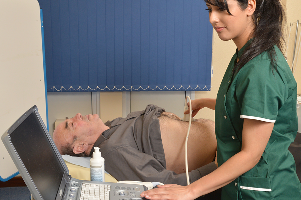 Photo of a screening technician performing an ultrasound scan test on a man who is lying down with his abdomen exposed