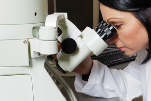 photograph: a woman in a white jacket using a microscope.