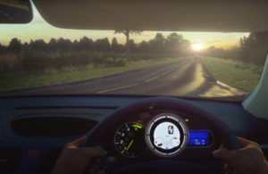 Computer generated imagery of the view from the driver's seat of a car, showing a road ahead, with a car travelling towards the driver