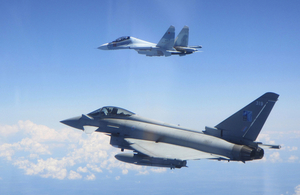 An RAF Typhoon jet flies alongside a Russian fighter jet against a bright blue sky