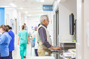A doctor stands at a computer desk in a busy hospital corridor.