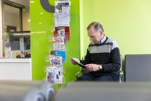 An older man sitting in a GP waiting area, reading a leaflet