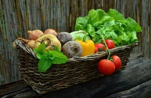 A basket of vegetables including lettuce, tomatoes and peppers in a brown basket.
