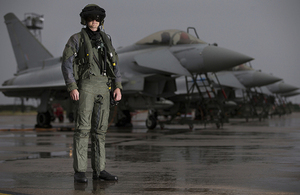 A pilot from 6 Squadron, RAF Lossiemouth stands in front of a line of Typhoon aircraft in full flying attire.