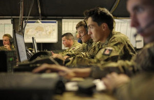 Image of battle headquarters with soldiers sitting at a desk some with headsets looking at computers.