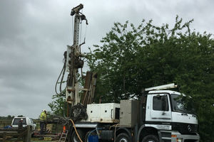 Flat-bed lorry with tall drill at rear to dig a borehole