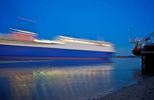 Cargo ship at dusk, passing close to shore, lights visible