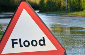 An image of a flood sign in front of a flooded road.