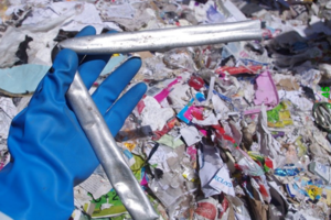 A hand in a blue glove holding a bent pipe with waste in the background