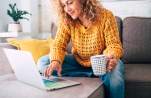 Woman sitting on sofa using laptop with cup in hand.