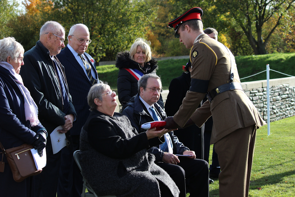 Lieutenant Piers Darby gives the Union Flag to Linda Cook, granddaughter of Lance Corporal Perkins