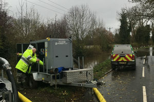 An Environment Agency officer operating a water pump next to a road with an EA vehicle parked nearby