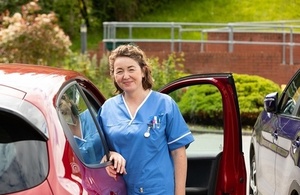 Nurse standing outside her car in a hospital car park