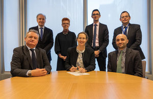 People standing and sitting around a table signing a contract