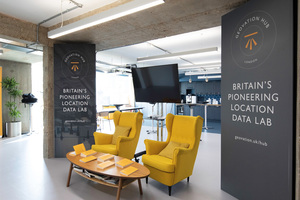 Two chairs and a desk in front of a screen and flanked by banners at the Geovation hub in London.