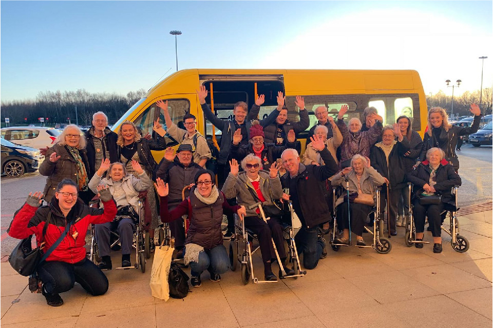 Photo of a group of people standing outside a yellow minibus purchased by the Denby Dale Centre as part of their volunteer car service.