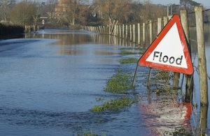 A flood warning sign on a closed country road next to water logged fields.