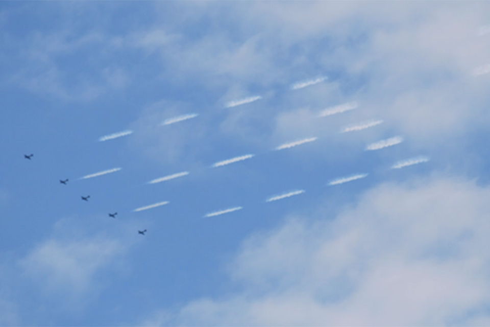 Image showing an example of skytyping by five aircraft flying in a line abreast formation, pictured against a blue sky background, releasing smoke in a coordinated manner which forms a pattern similar to dot printing.