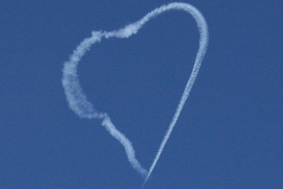 Image showing a skywriting contrail design completed by white smoked released against a blue sky background in the shape of a love heart.