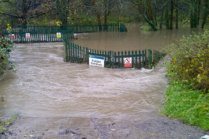 Flood water swamping a compound with green fence and signage visible