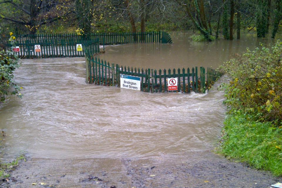 Flood water swamping a compound with green fence and signage visible
