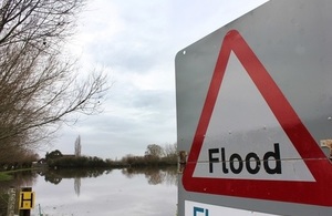 UK flood sign overlooking flooded land in rural area.
