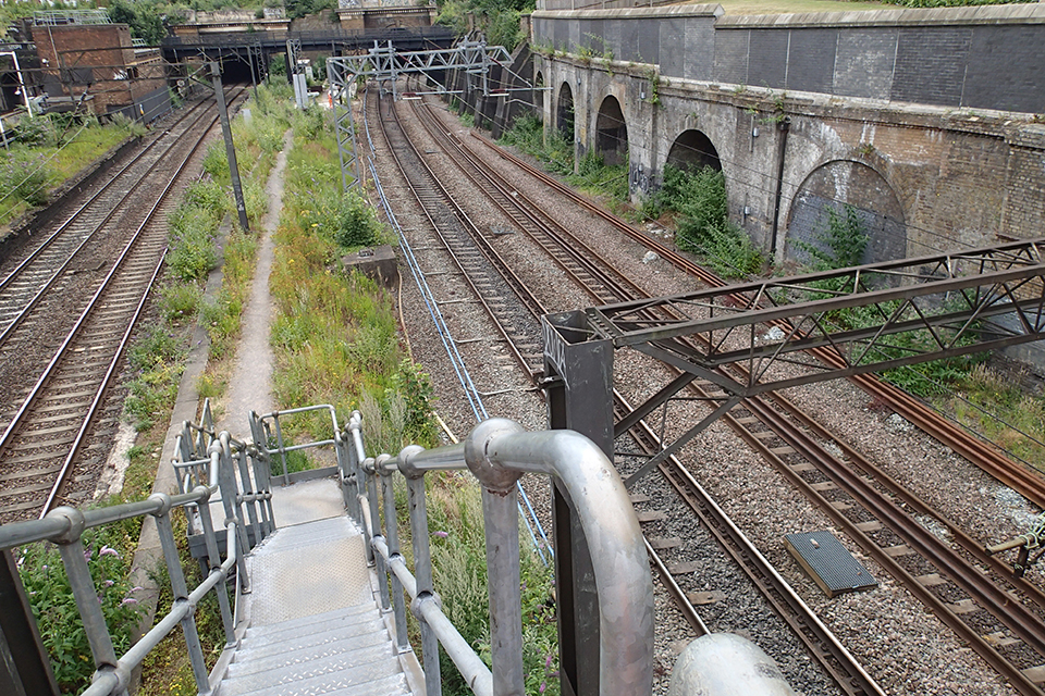 View from an overbridge of two sets of lines at South Hampstead from the access steps. Railway arches on on the right with two sets of overhead line gantries.