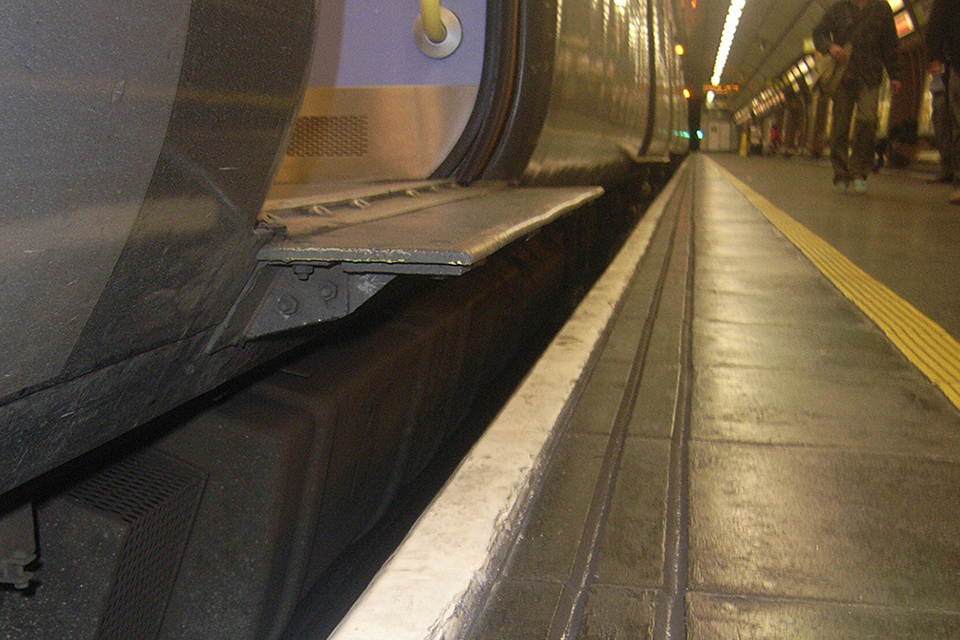 Low level view from the platform edge showing the train doors, step, gap and platform. The platform edge has a white strip and grooved tactile marks.