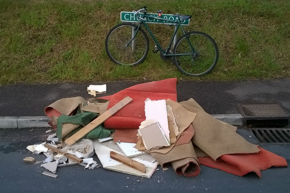 Photo of bicycle leaning against road sign and carpets dumped on pavement