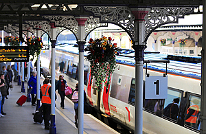 Rail station platform with passengers and hanging baskets of flowers.