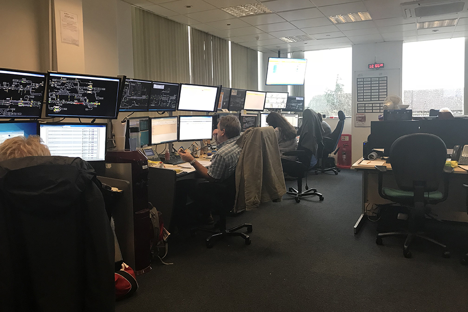 The control room of a train operating company. Operators are seating at workstations with banks of screens giving them train information.