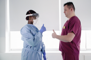 Two professionals in a clinical setting wearing PPE.