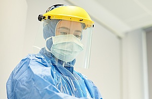 Healthcare worker wearing full PPE including face mask, visor, apron and long sleeved gown with hood