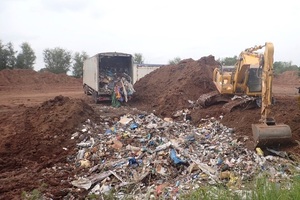 A bulldozer moving waste in front of a pile of soil and an articulated lorry full of waste