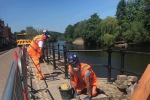 Two workmen maintain stone flood defences by the side of the river Severn