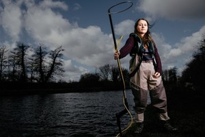 A female Environment Agency employee stands with an electro-fishing rod by a lake