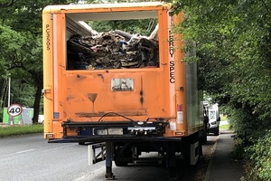 An orange lorry trailer full of waste, parked in a road layby