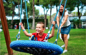 Boy swinging as he is pushed by a woman