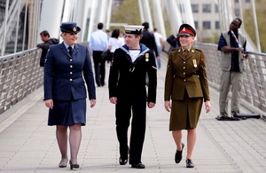 From left to right; woman in Royal Air Force uniform walking alongside a man in Navy uniform and a lady in British Army uniform on the right hand side.