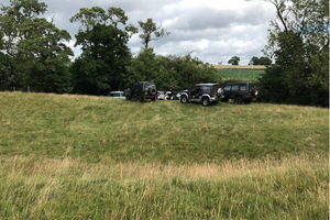 A group of 4x4 vehicles parked in a field next to a river