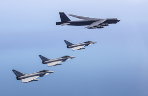 Typhoons escorting two B52 bombers in front of a blue sky.