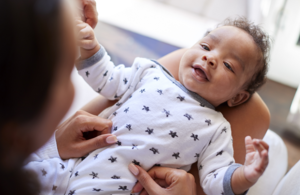 Happy 3-month-old baby boy lying on his back on his mother's knee looking up at her