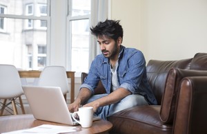 Photo of a man, sat on a sofa, using a laptop