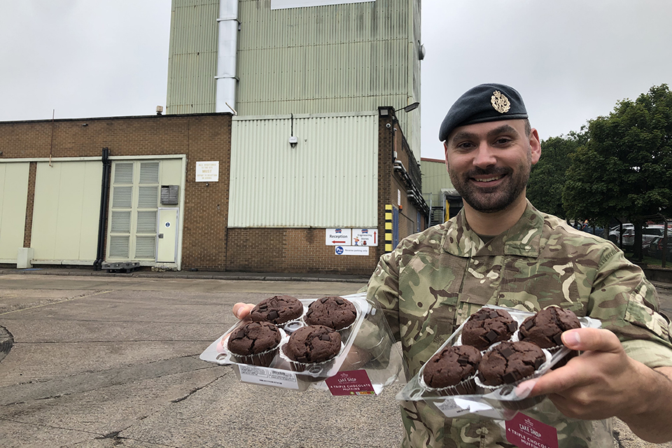 RAF Reservist Danny Railton holding trays of muffins and smiling at the camera. 