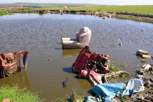 Picture of arm chair, carpet and other items of rubbish sat in a hilltop pond