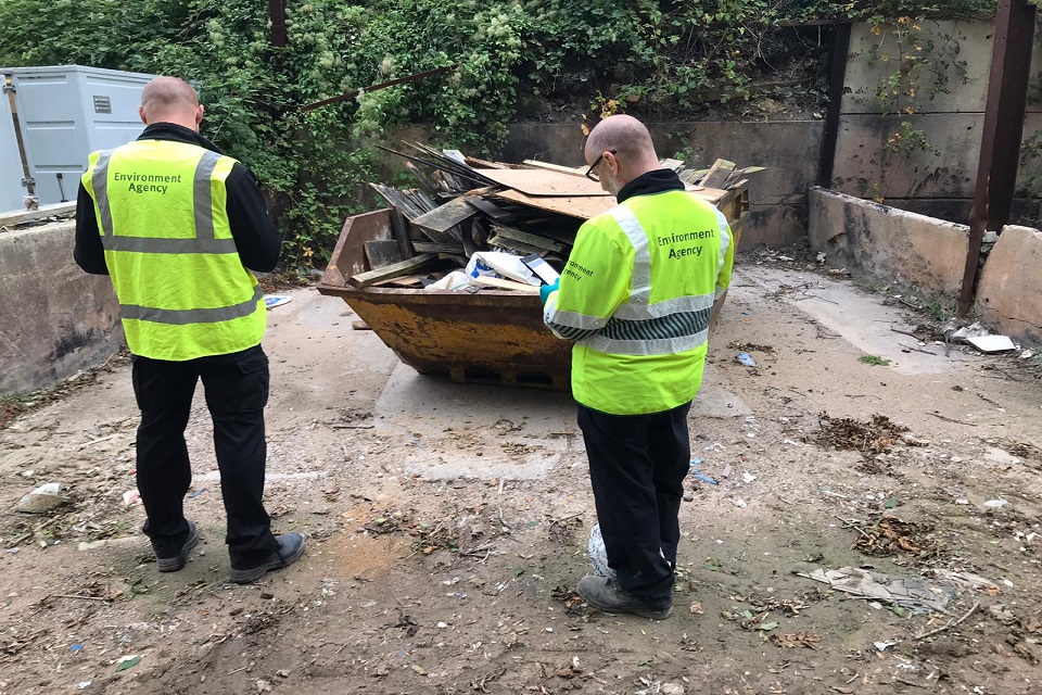 Officers looking at a skip full of waste and taking notes.